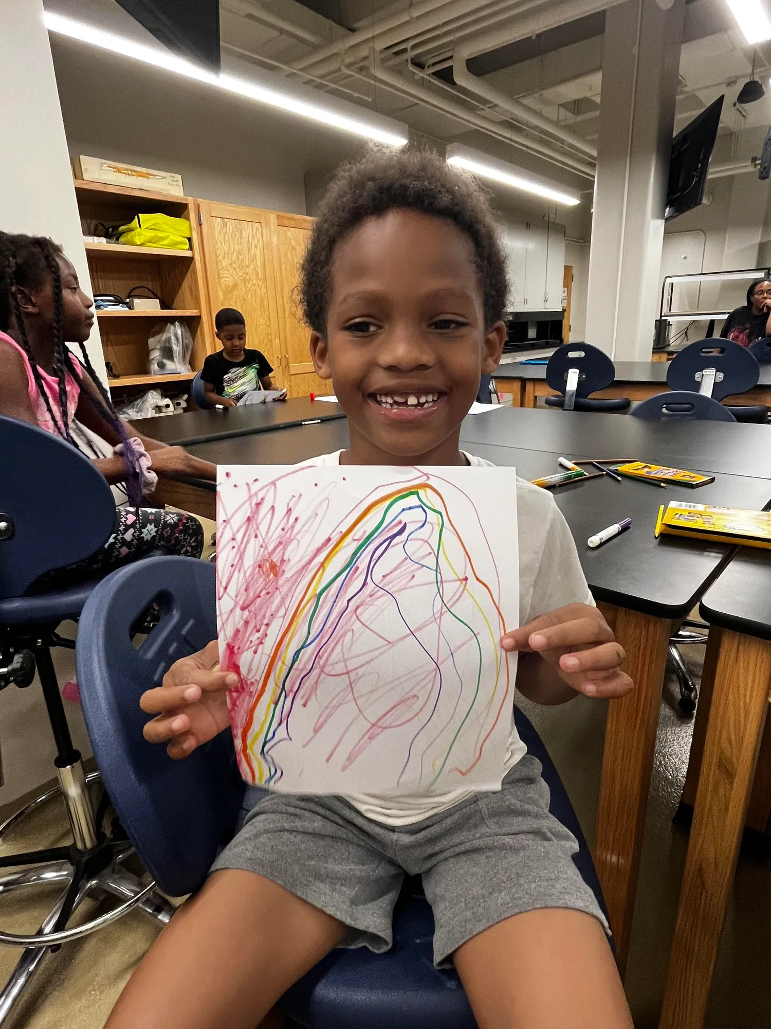 Youth participant proudly displaying their rainbow artwork during a program activity